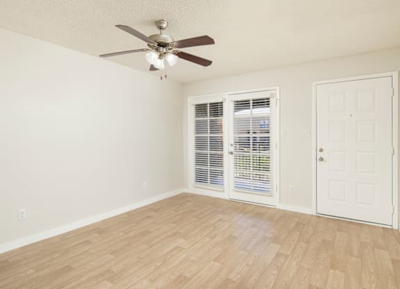 A room with a ceiling fan and sliding glass doors.