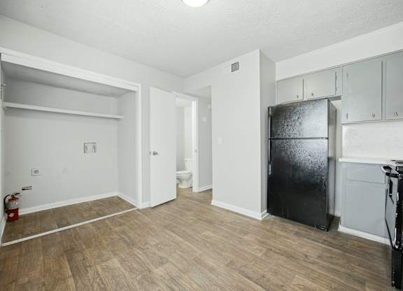 A room with a black fridge and wooden floors.