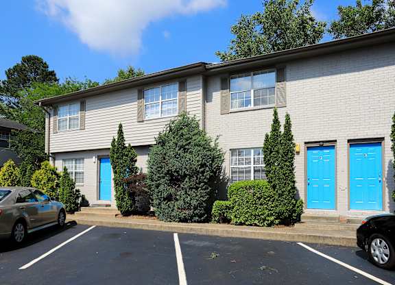 A building with blue doors and windows is surrounded by trees and cars.