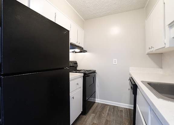 A black refrigerator is in a kitchen with white cabinets.
