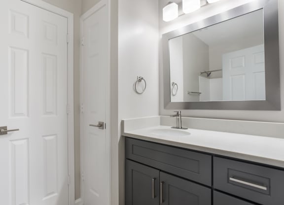 A bathroom with a white door, a mirror, and a sink.