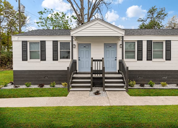 the front of a white house with blue doors and a porch