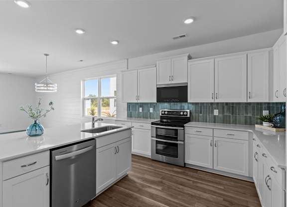 A modern kitchen with white cabinets and a wooden floor.