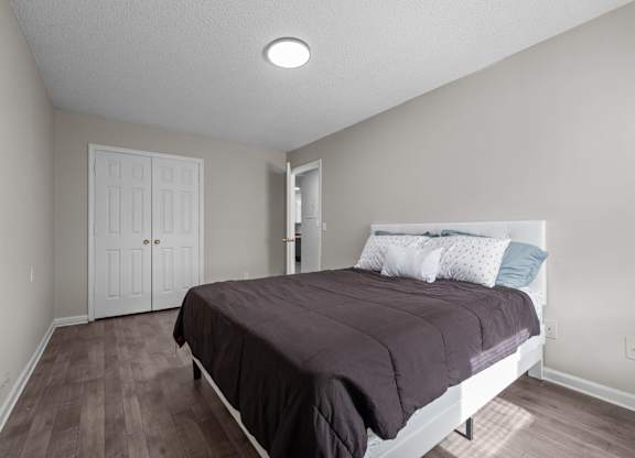 A bedroom with a bed, pillows, and a wooden floor.