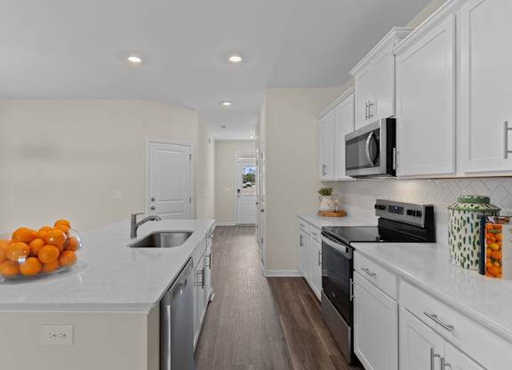 A kitchen with white cabinets and a countertop with oranges on it.