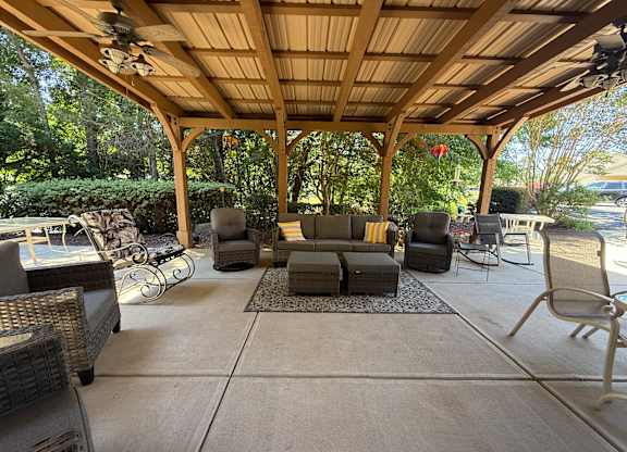 A covered patio with a couch, chairs, and a fan.