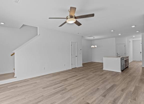 A room with a ceiling fan and light fixture, a staircase, and a kitchenette.