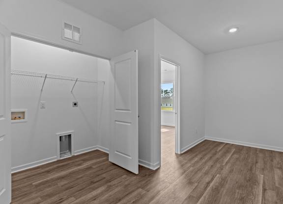 A white room with wood flooring and a doorway leading to another room.