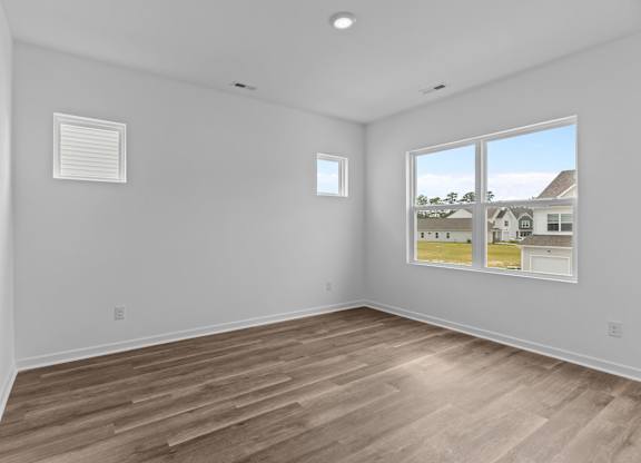 A room with wooden flooring and two windows.