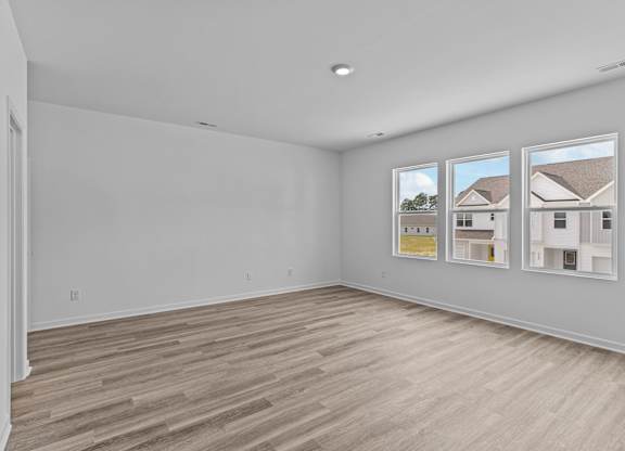 A large empty room with wood flooring and three windows.