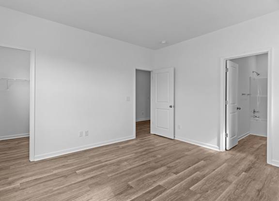A room with white walls and wooden flooring with four doors.