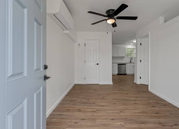 an empty living room with a ceiling fan and a kitchen