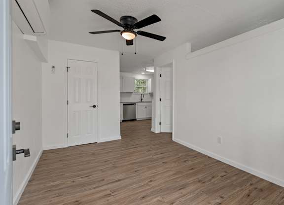 an empty living room with a ceiling fan and a kitchen