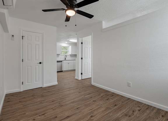 an empty living room with a ceiling fan and a kitchen