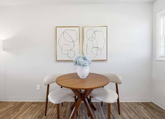 A table with chairs and two framed pieces of artwork on the wall.