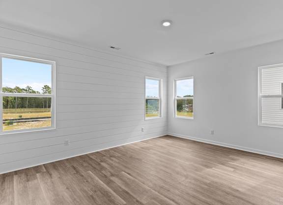 A room with wooden floors and white walls with two windows.