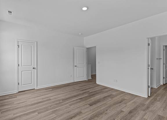 A room with white walls and wooden flooring with four doors.