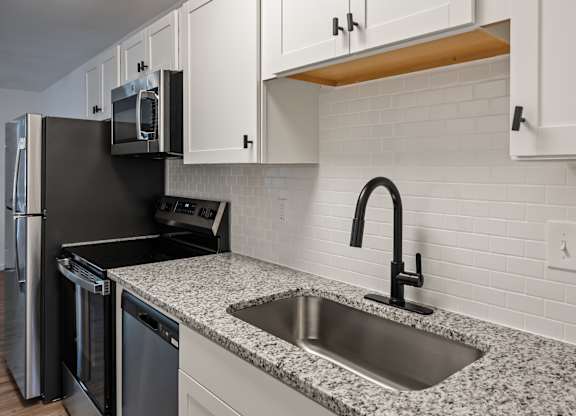 A kitchen with a black refrigerator and a granite countertop.