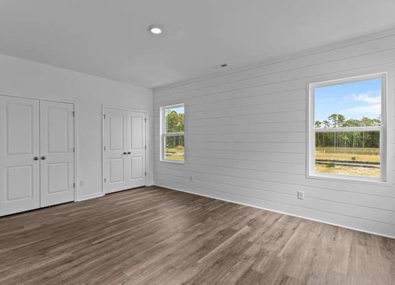 A room with white walls and wooden flooring with a window showing a view of trees.