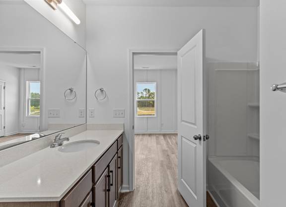 A white bathroom with a sink, mirror, and a door leading to another room.