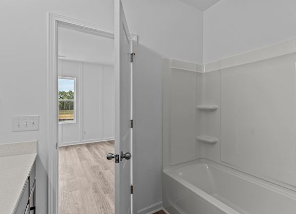A white bathroom with a tub and a doorway leading to another room.