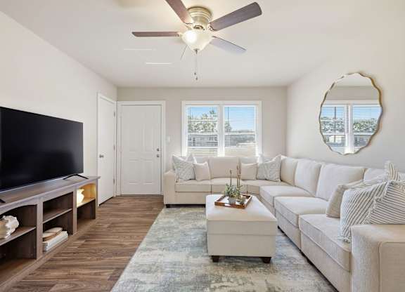 A living room with a white couch, a television, and a ceiling fan.