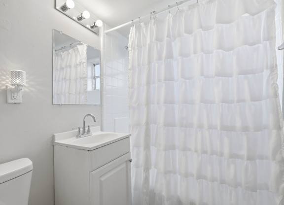 A white bathroom with a white sink and a white shower curtain.