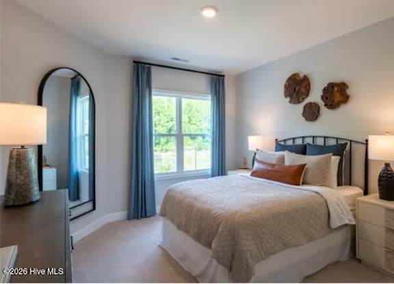 A bedroom with a large bed, a mirror, and a window with curtains.