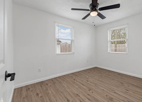 an empty room with a ceiling fan and two windows
