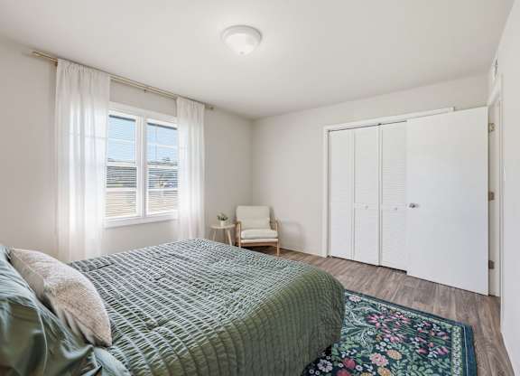 A bedroom with a bed, chair, and a window.