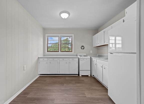A white kitchen with wood flooring and white cabinets.