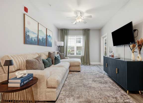 A living room with a large couch, a coffee table, and a flat-screen TV mounted on the wall.