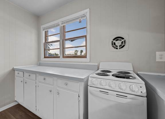 A white kitchen with a stove and a window.