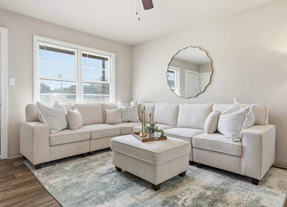 A living room with a white couch and a round mirror on the wall.