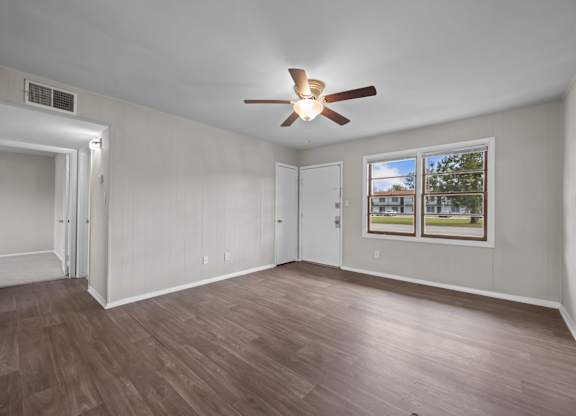 A room with a ceiling fan and a window showing a view of a house and trees.