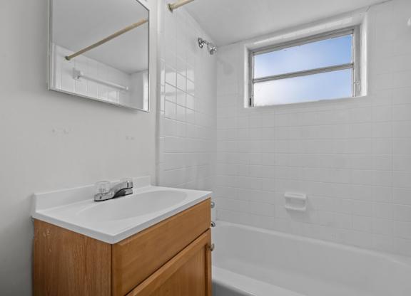 A white bathroom with a wooden vanity and a window.