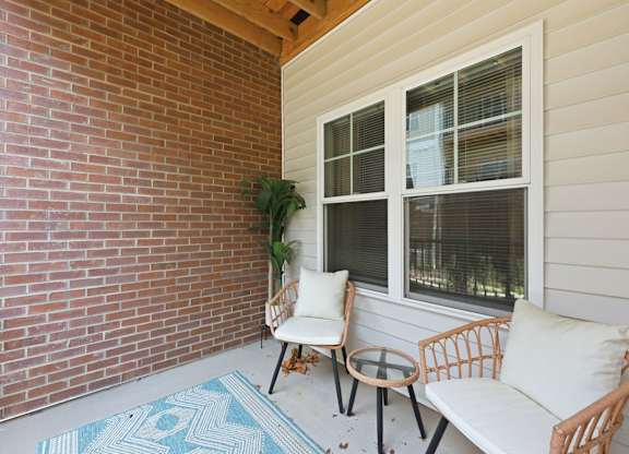 A patio with a white couch, two chairs, and a table with a potted plant.