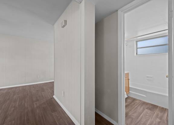 A room with white walls and wooden flooring with a doorway leading to another room.