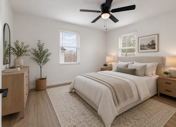 A bedroom with a large bed, a ceiling fan, and a plant on the side table.