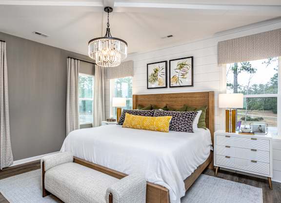 A bedroom with a large bed, a chandelier, and a window with curtains.