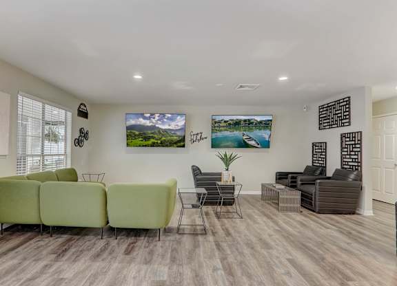 A living room with a green sofa, a grey sofa, a black chair, and a TV mounted on the wall.