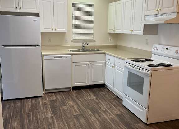 A kitchen with white appliances and wooden floors.