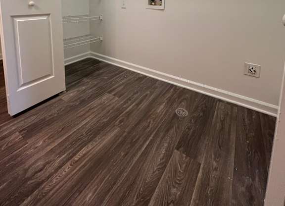 A white door is on the left of a room with a shelf and a light switch.