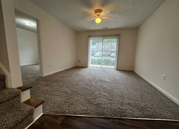 A room with a carpeted floor, a ceiling fan, and a window with blinds.