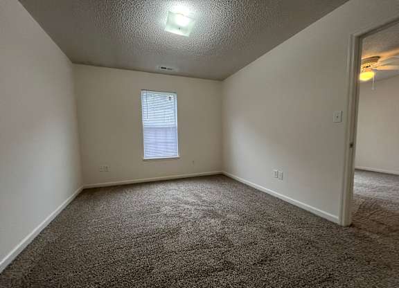 A room with a carpeted floor and a window with blinds.