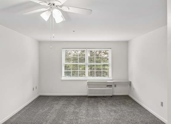 A room with a ceiling fan and a window with a view of trees.