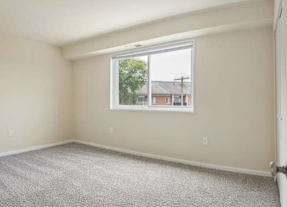 A room with a carpeted floor and a window showing a view of a residential area.