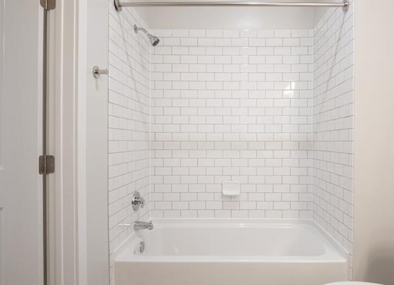 A white tiled bathroom with a bathtub and shower.