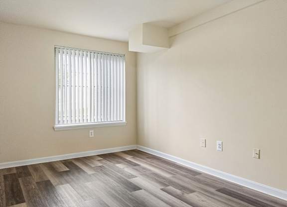 A room with wooden flooring and a window with blinds.