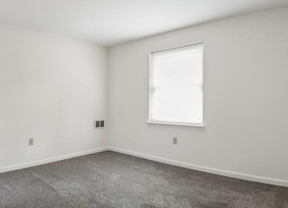 A room with a window and a carpeted floor.